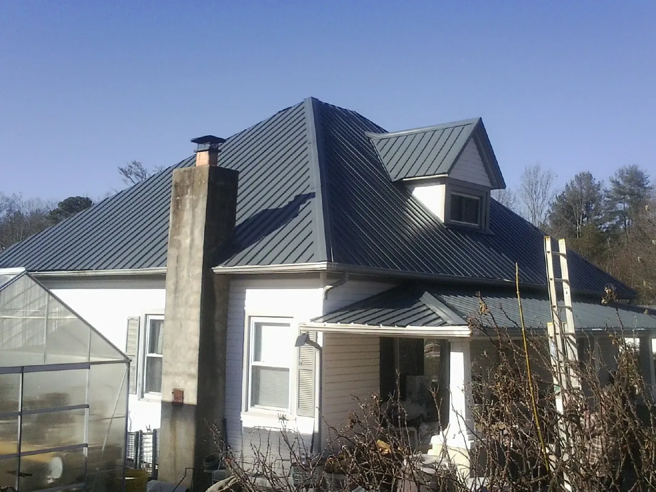 Dark blue standing seam metal roof on a white farmhouse with dormer — Slate & Tile Roof Repair by Roofing Brothers in Grizzly Flats