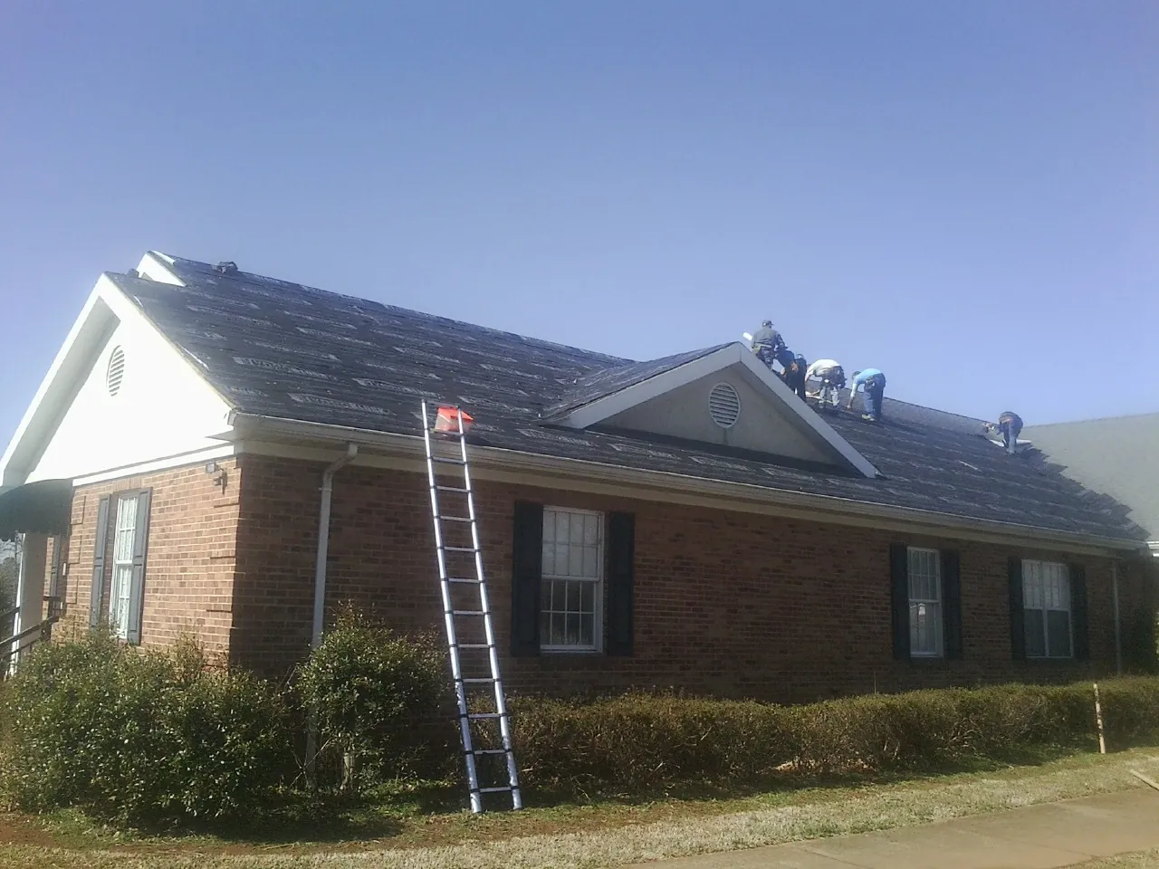 Crew tearing shingles off a brick ranch roof with a ladder set — Emergency Roof Repair work by our crew in Grizzly Flats