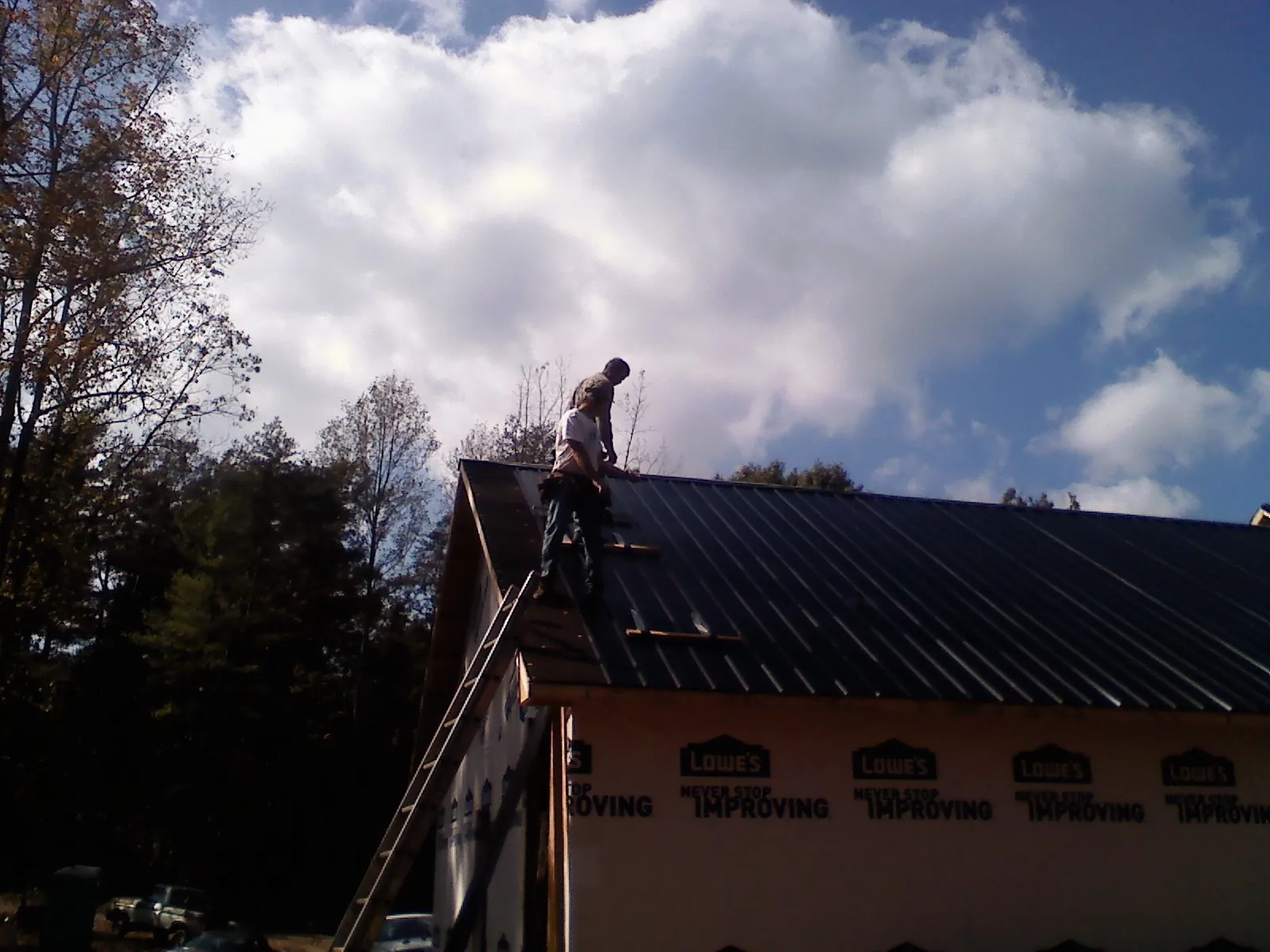 Roofer fastening dark metal panels high against a cloudy sky, from a Roof Inspection job in Grizzly Flats