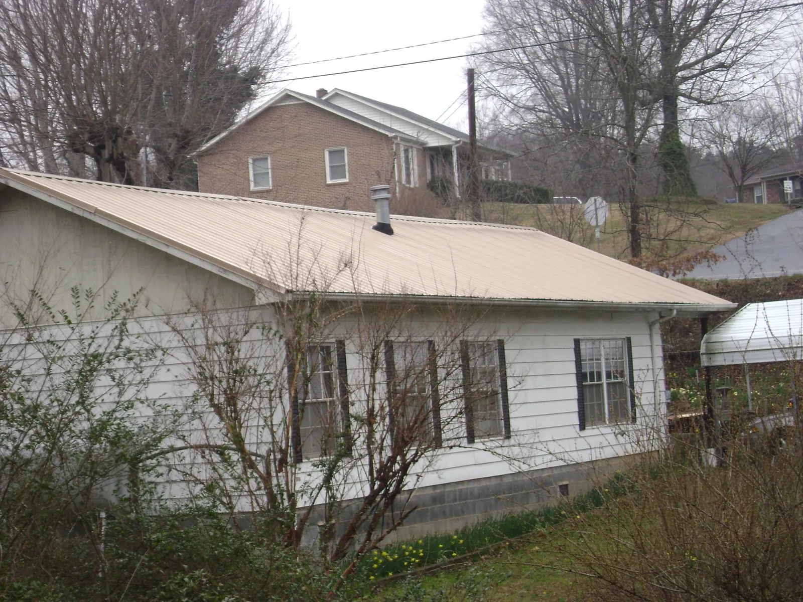 Tan metal roof on a white sided house set into a hillside — Commercial Roofing by Roofing Brothers in Grizzly Flats