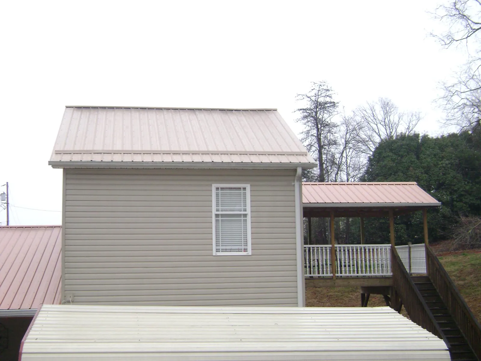 Tan metal roofs on a two story addition and attached porch, from a Roof Replacement job in Grizzly Flats